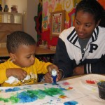 Teen volunteer Cameron works with Wilson on his painting