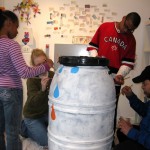 The Taylor family works with Art Mentor Mindy Fisher on "It's Raining cats and Dogs" rain barrel.